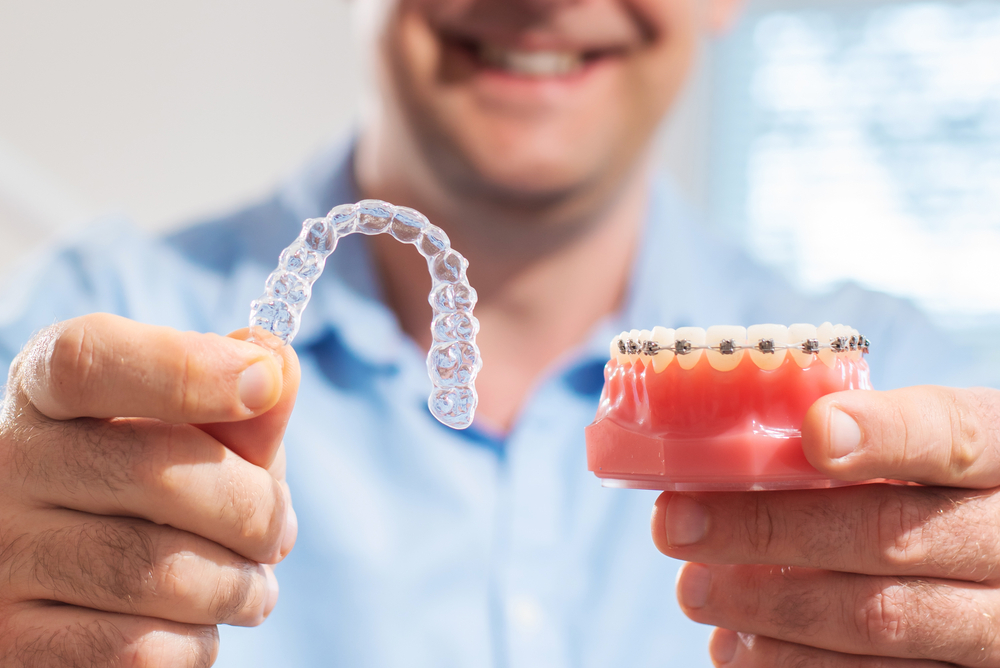 Dental care.Smiling dentist doctor holding aligners and braces in hand shows the difference between them